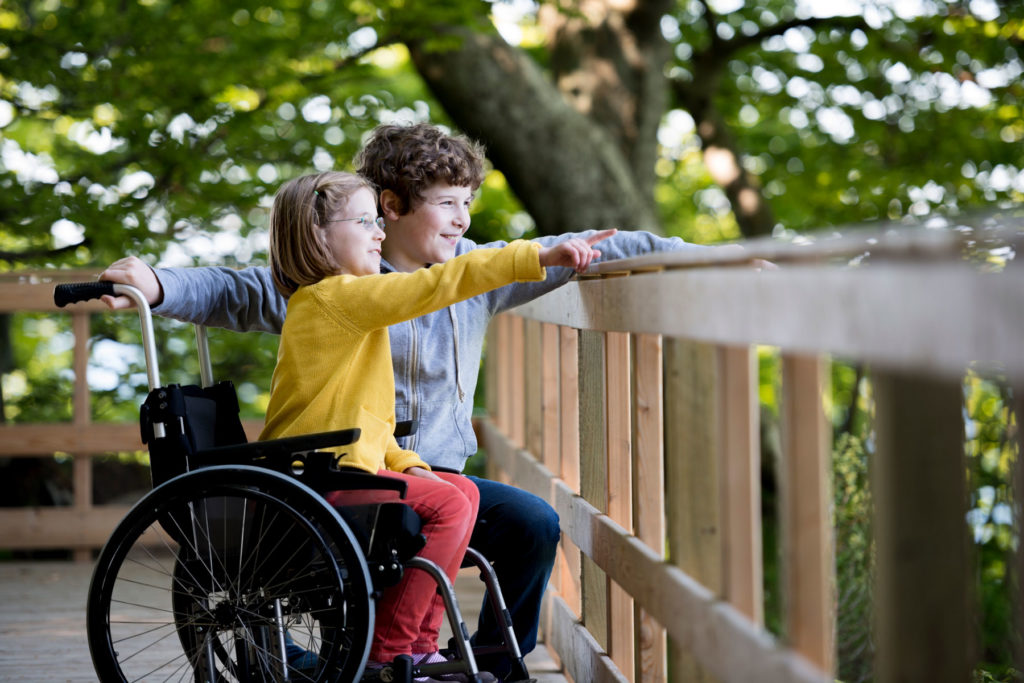 image d'une jeune fille en fauteuil roulant montrant une jeune boîte à côté d'elle en souriant