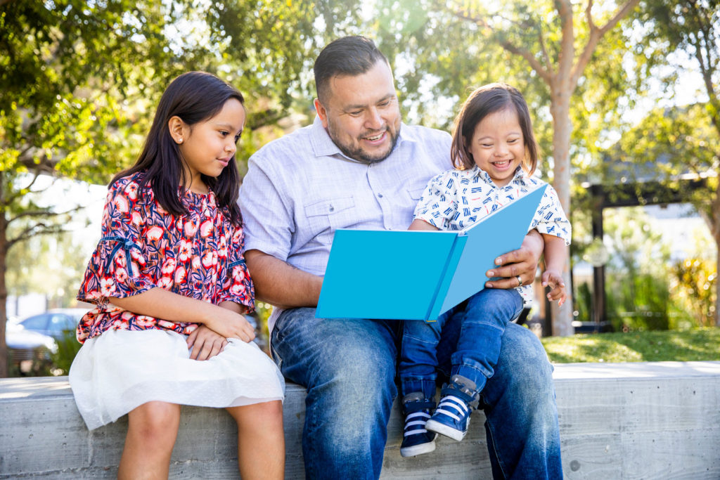 imagen del padre leyendo un libro a un niño pequeño en su regazo y joven a su lado