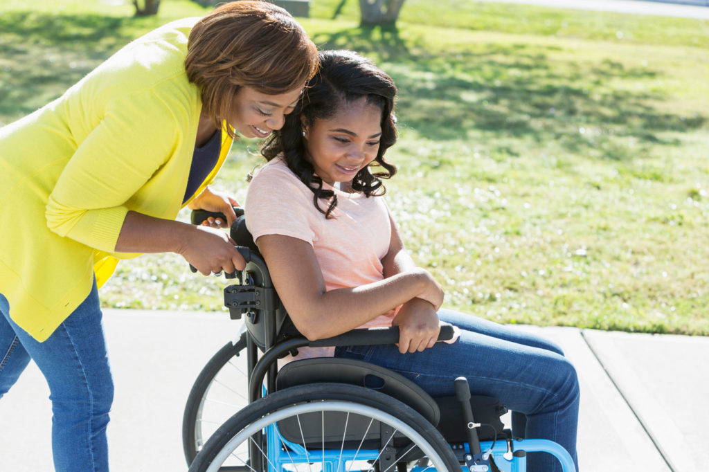 Bild von Teenager-Mädchen im Rollstuhl, das von ihrer Mutter geschoben wird