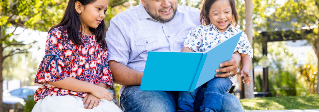 image of father reading a book to a toddler on his lap and young beside him
