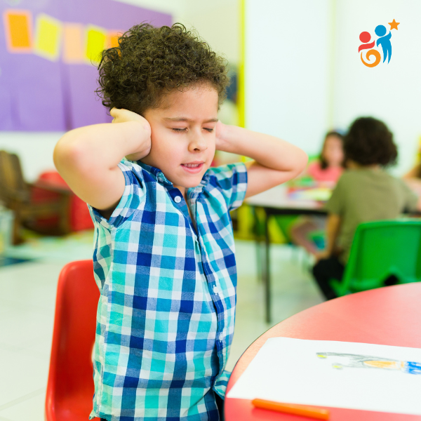 Child in a classroom standing up and covering his ears with his hands