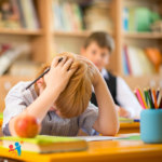 Young boy at a classroom desk with his hands on his head and looking down in frustration
