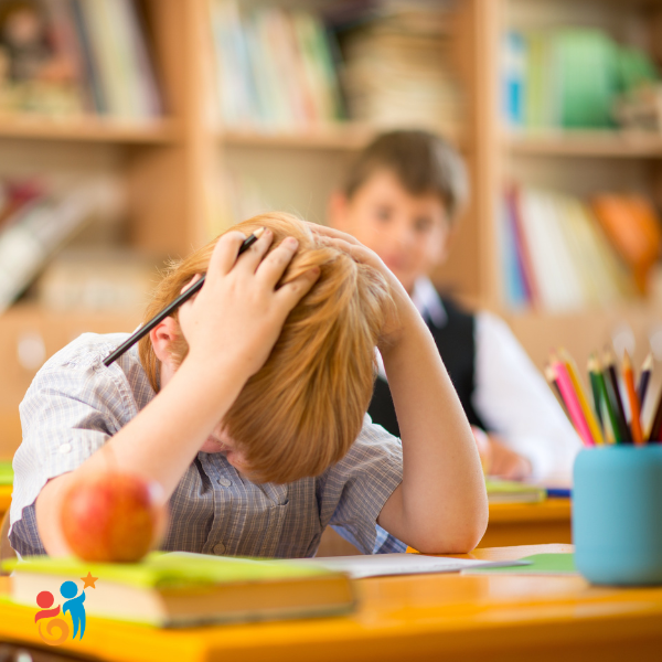 Young boy at a classroom desk with his hands on his head and looking down in frustration