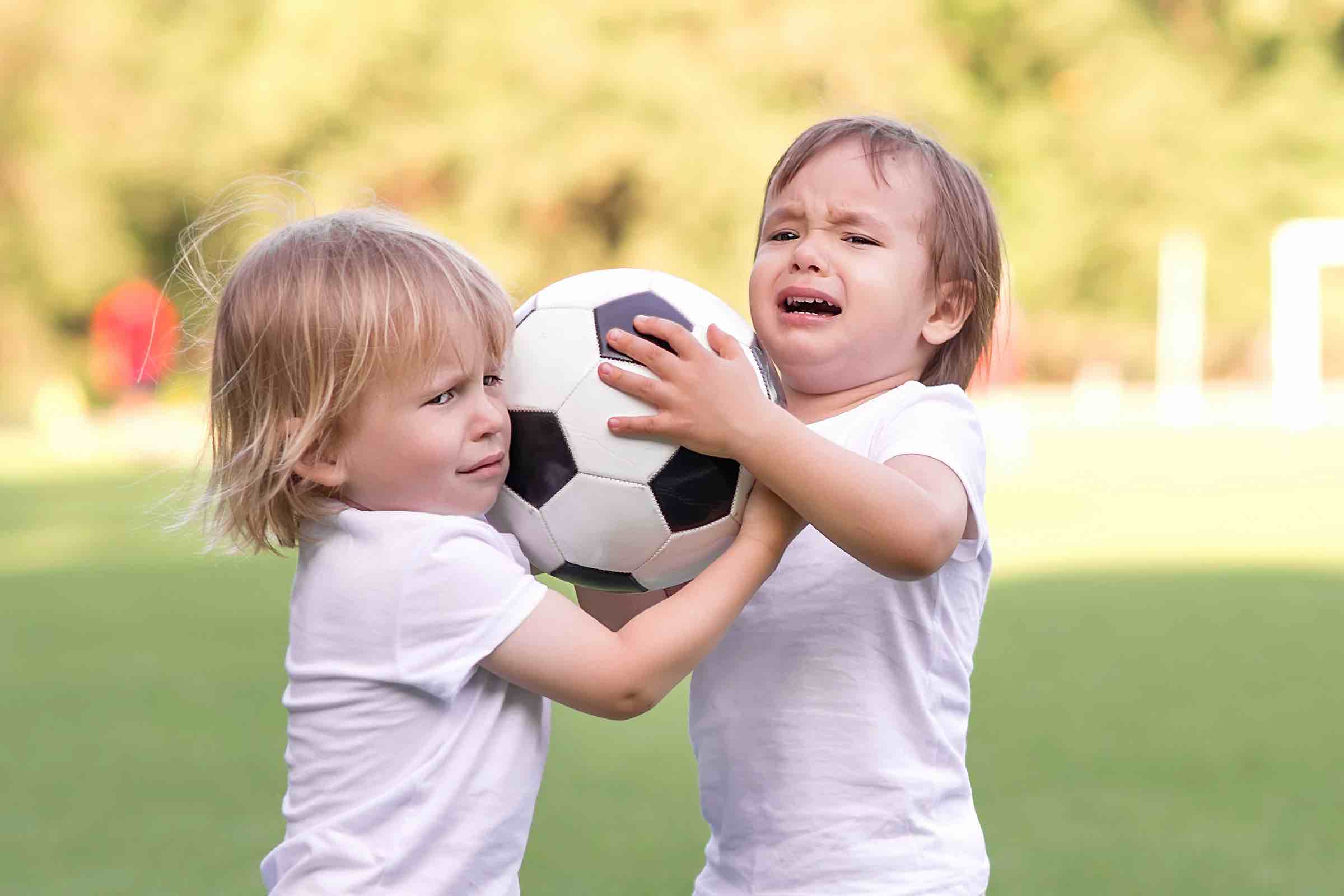 Two little toddlers arguing at football field or playground over soccer ball trying to take or grab ball. Conflict management, corporate fight metaphor and conflict resolving concept. Copy space