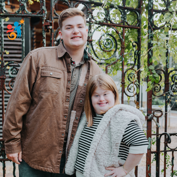 Brother and sister standing next to a metal fence smiling