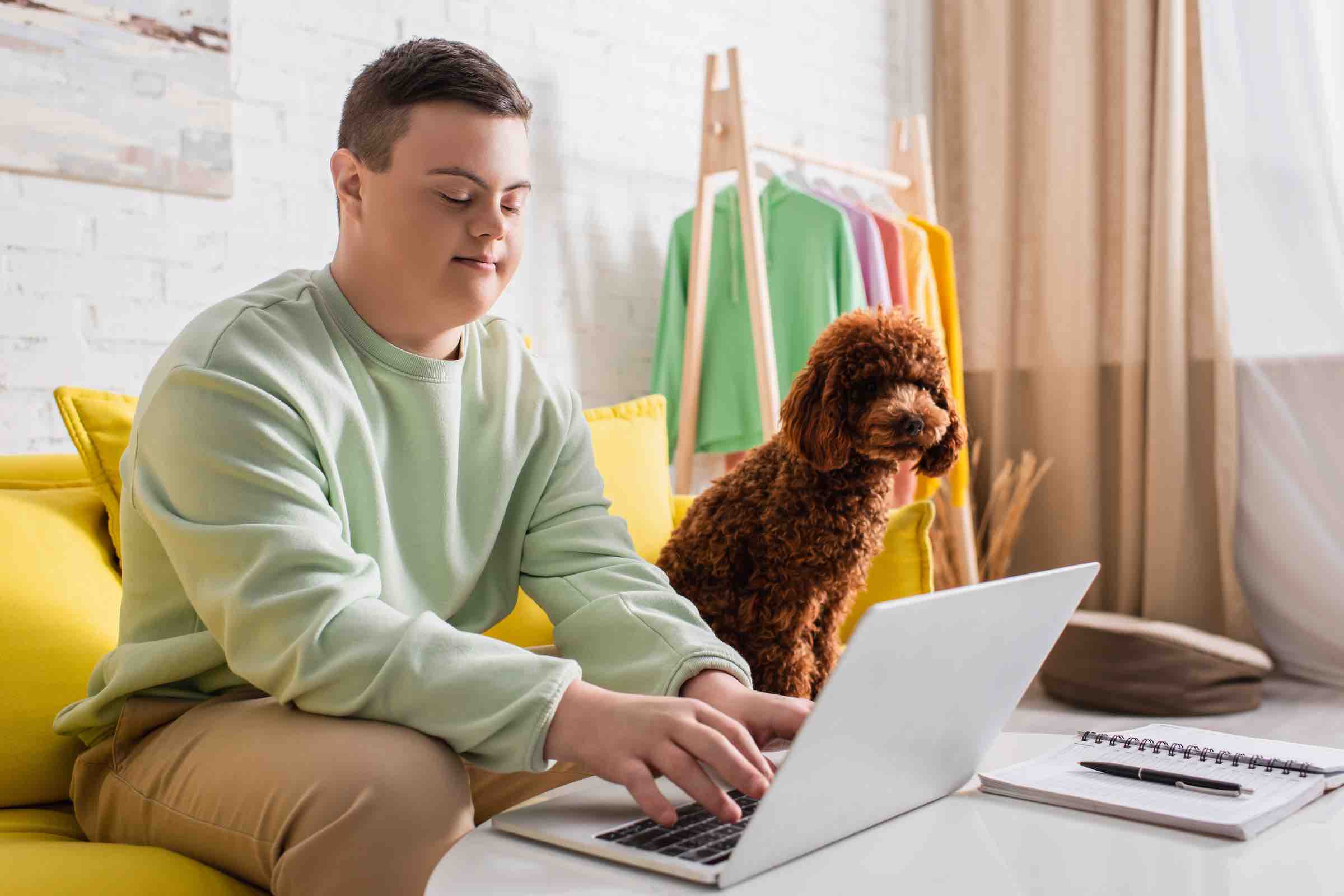 special needs male working on laptop with dog on couch