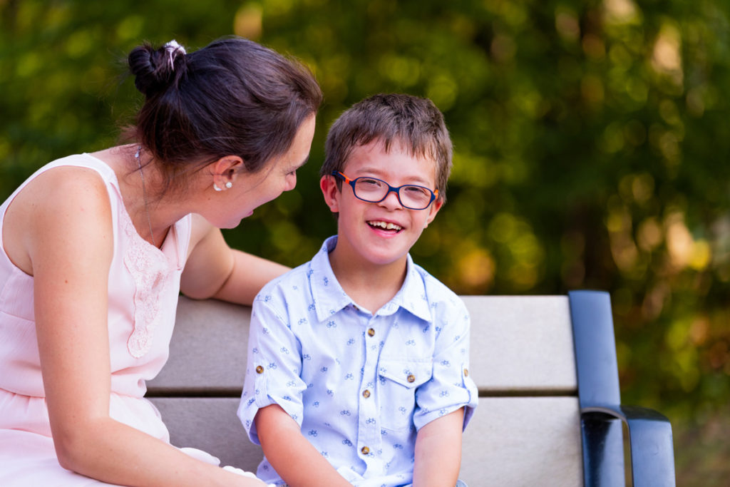 Bild von kleinen Jungen mit Brille sitzt neben Mama auf Parkbank