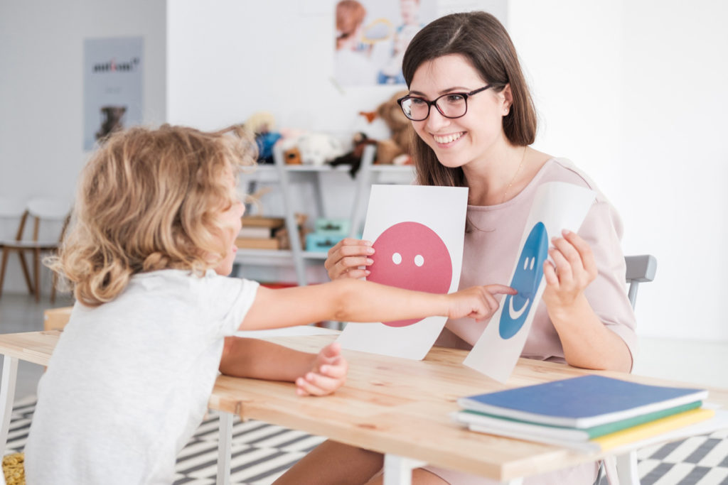 Bild eines Kindes, das eine Wahl trifft und auf ein Smiley-Gesicht zeigt, das die Lehrerin in der Hand hält