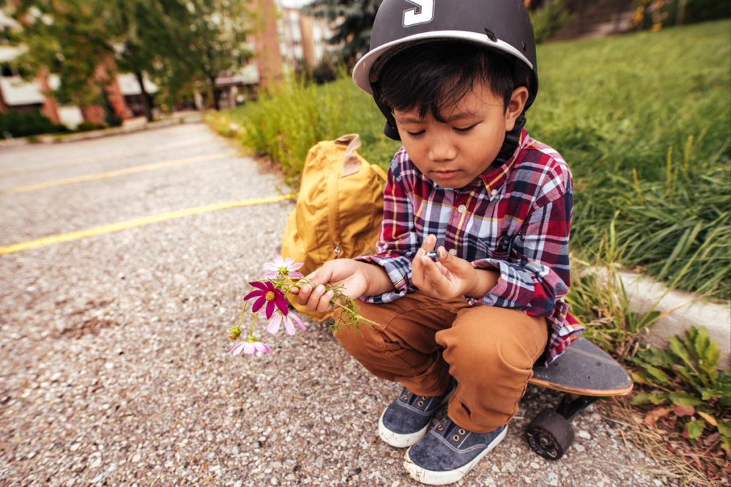 Bild eines Jungen mit Helm, der auf einem Skateboard sitzt und Blumen hält