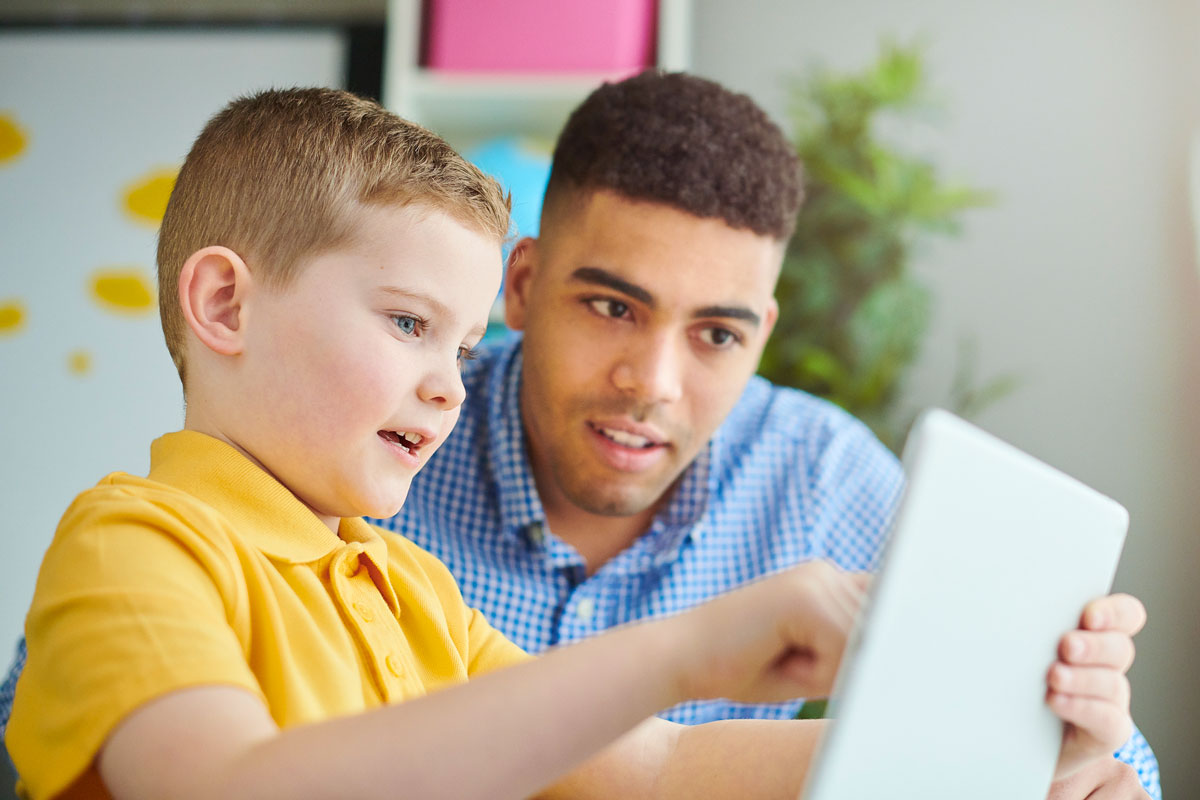 Child reading on tablet device with teacher