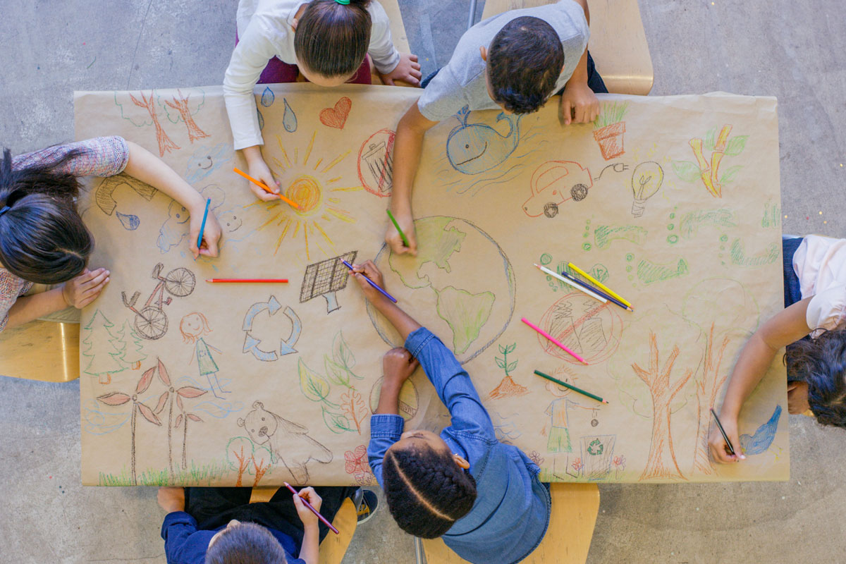 Verschiedene Gruppen von Kindern, die mit Buntstiften auf einem Tisch im Klassenzimmer zeichnen