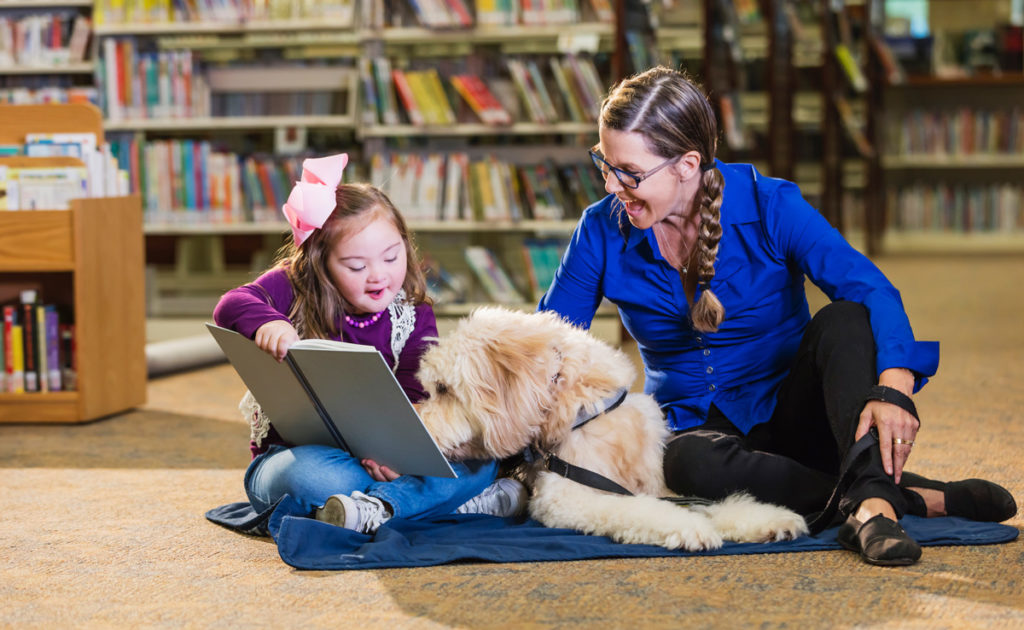 image of young girl reading book to adult female with service dog