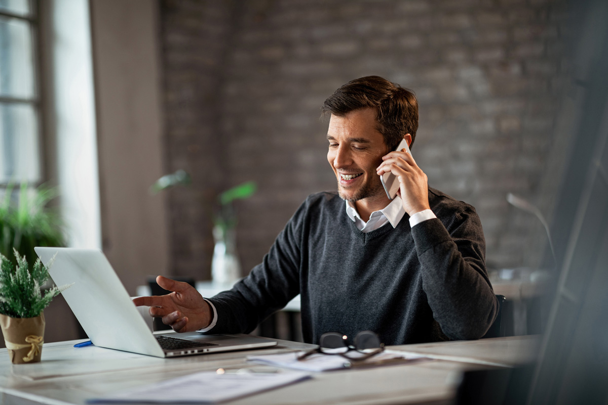 image of man on phone smiling with laptop open