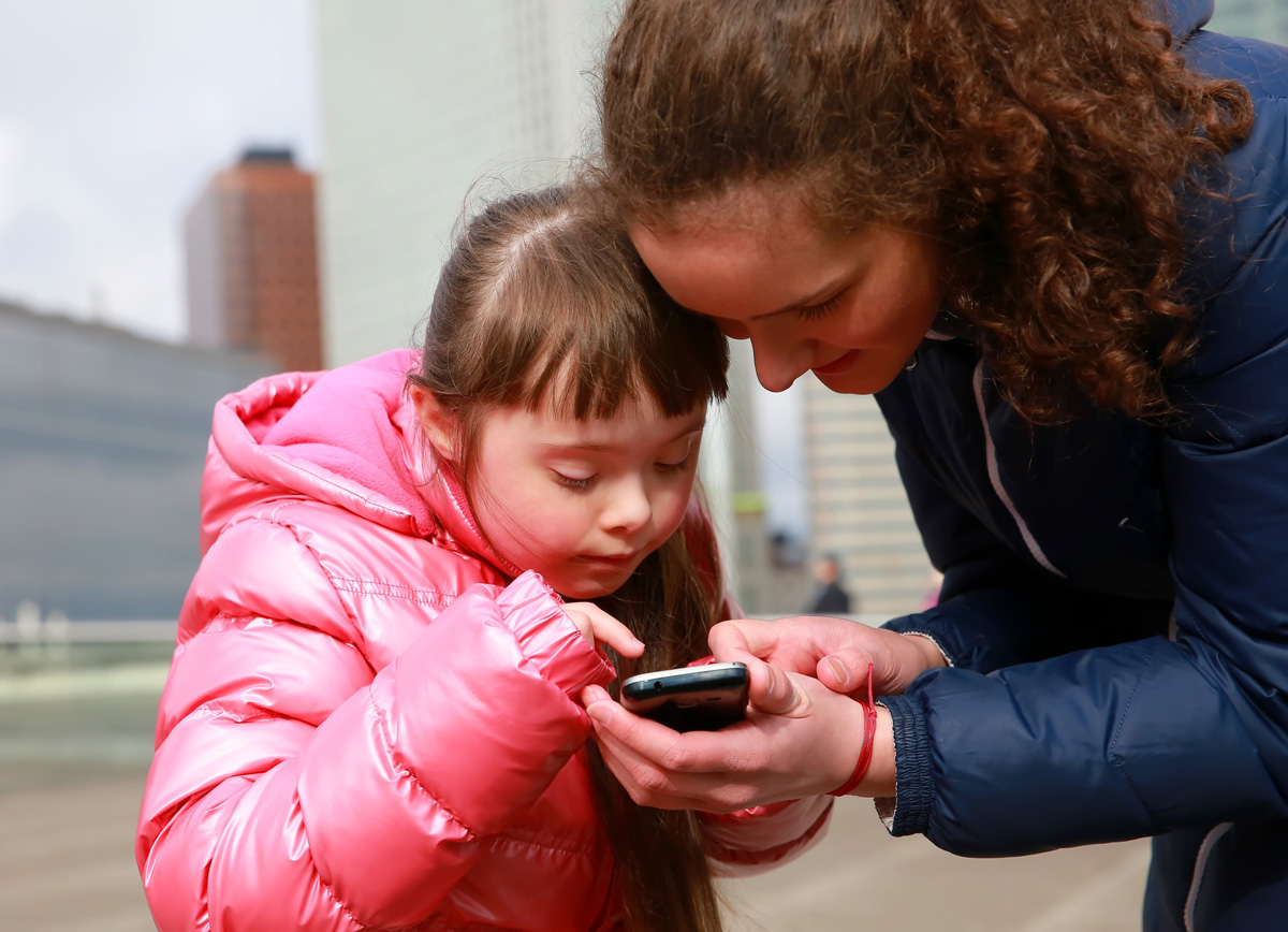 image of mother showing phone to young daughter with Down Syndrome
