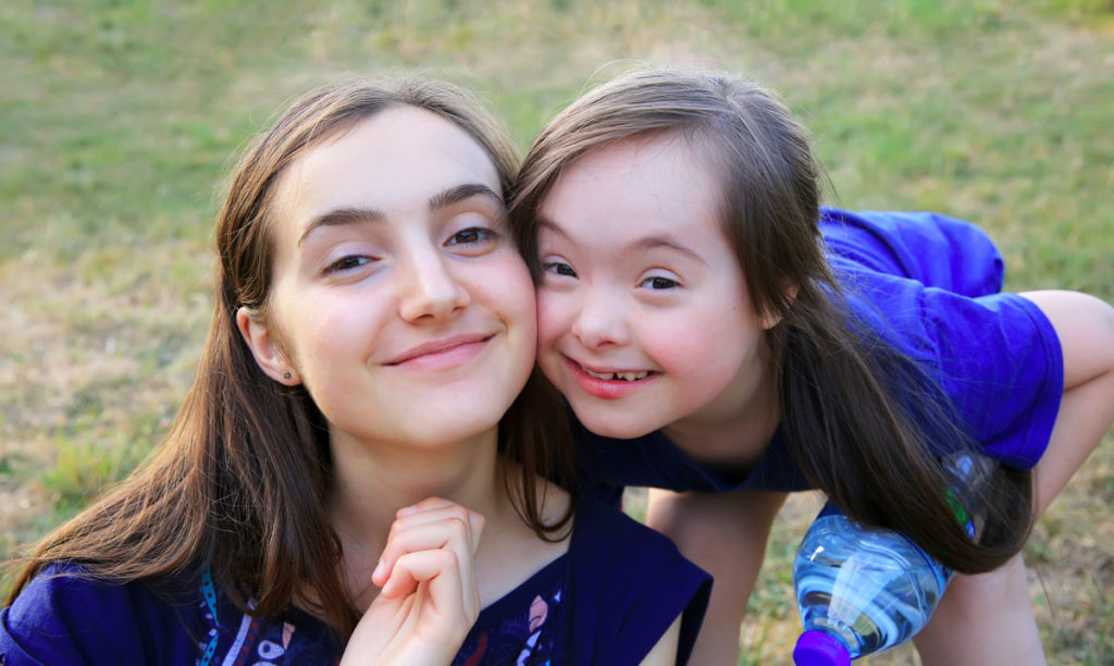 صورة لفتاة صغيرة مع متلازمة داون متكئة على كتف الأخت الأكبر