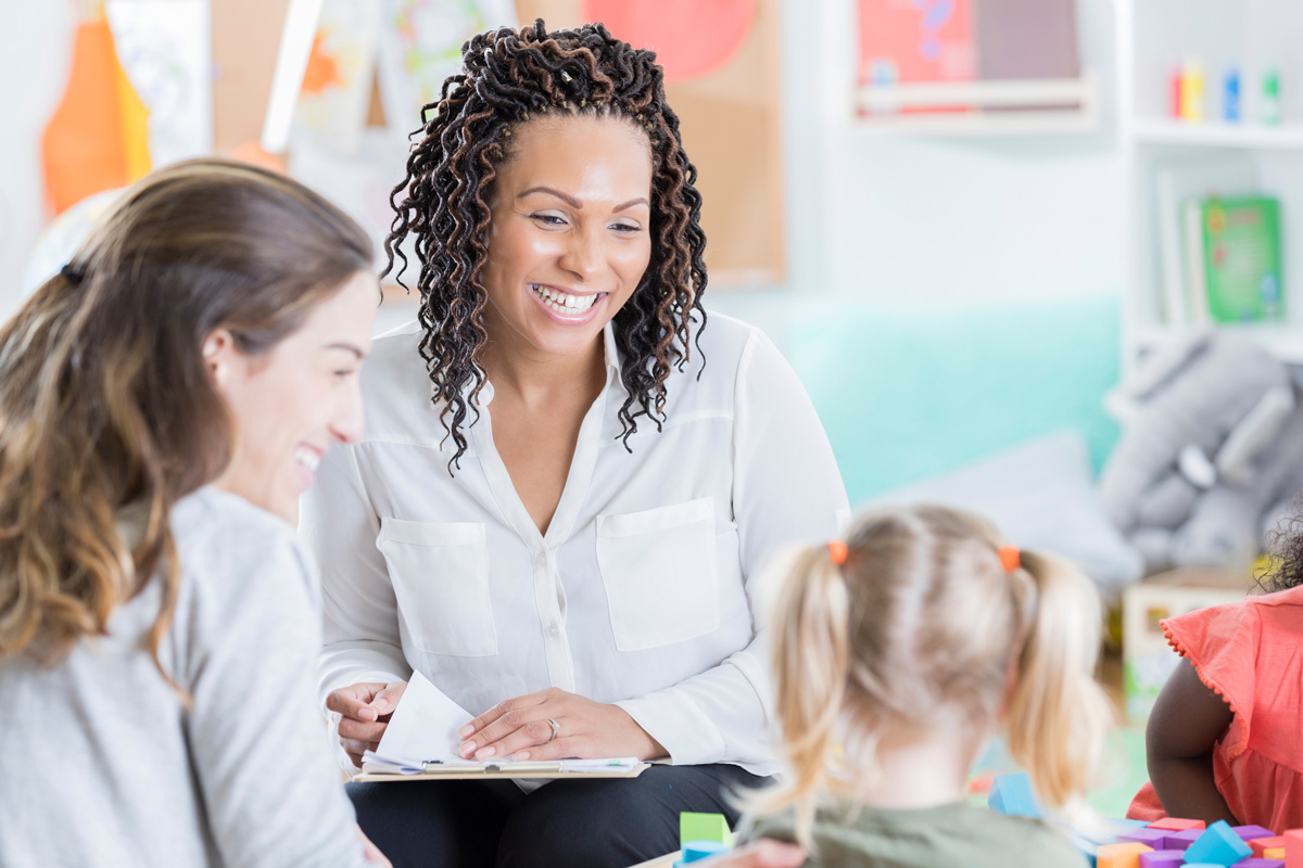 image of teacher smiling at toddler seated next to mother