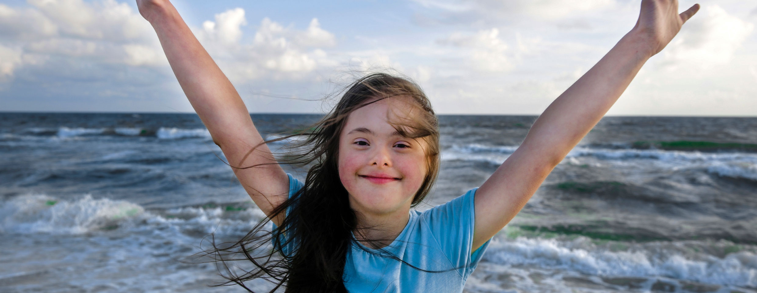 Young girl with arms raised at beach, smiling