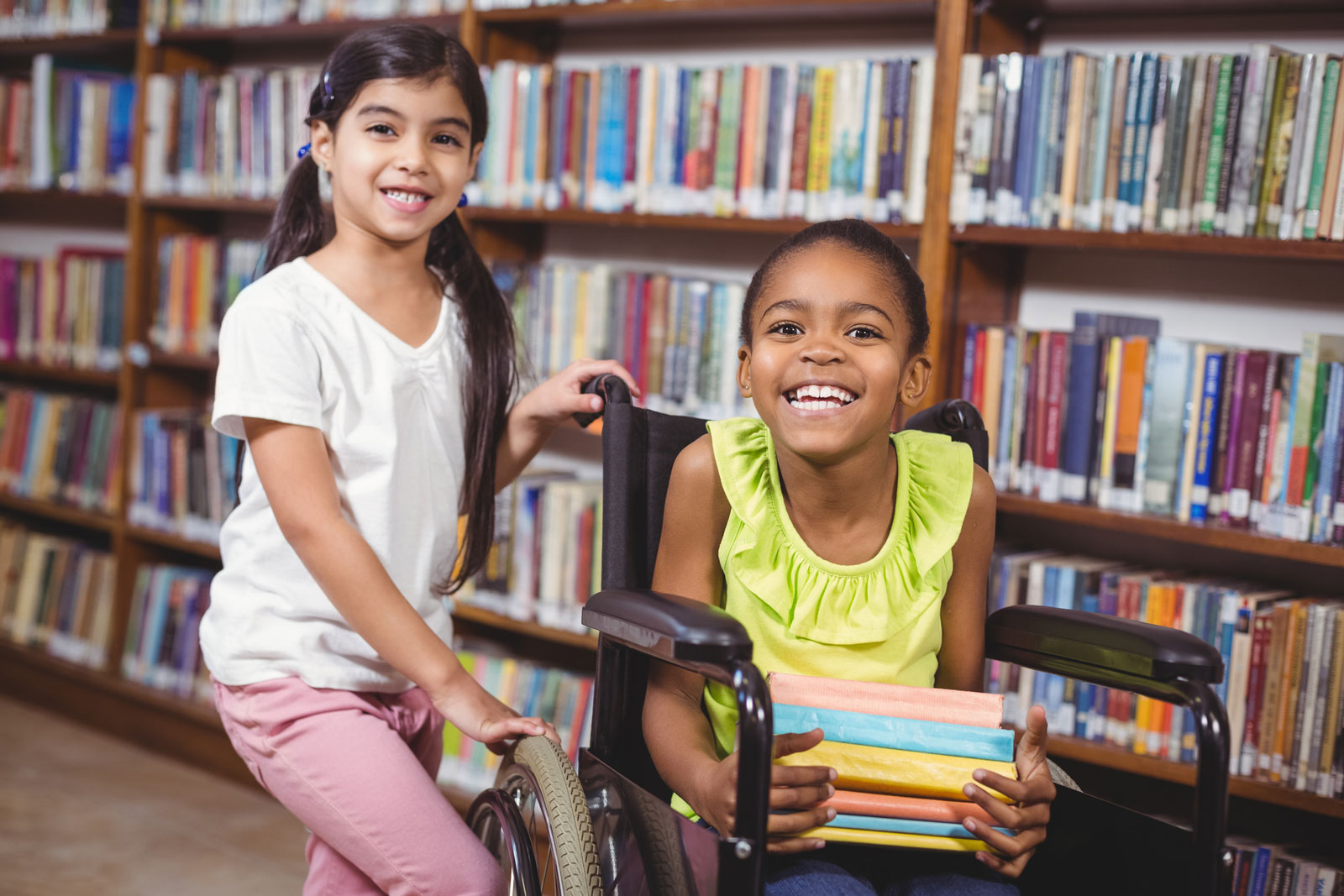 two female students in library, smiling, with books