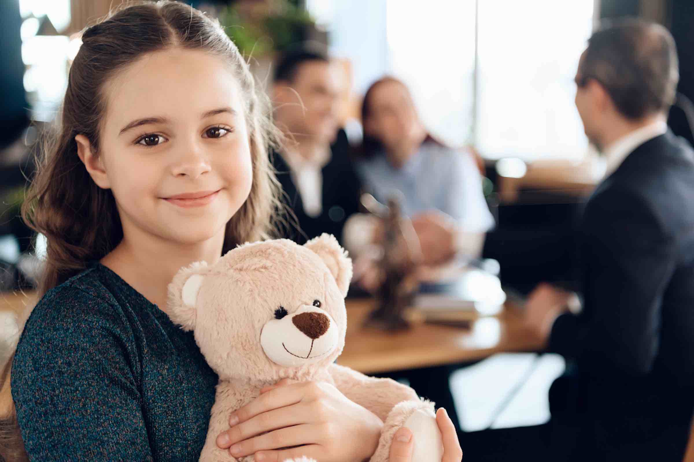 child with teddy bear with guardians in the background
