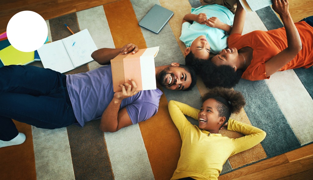 black dad, mom, daughter and son lying on a rug with school materials around them